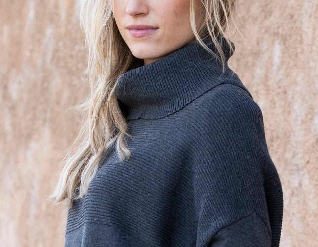 Person wearing a dark gray turtleneck sweater against a beige wall.