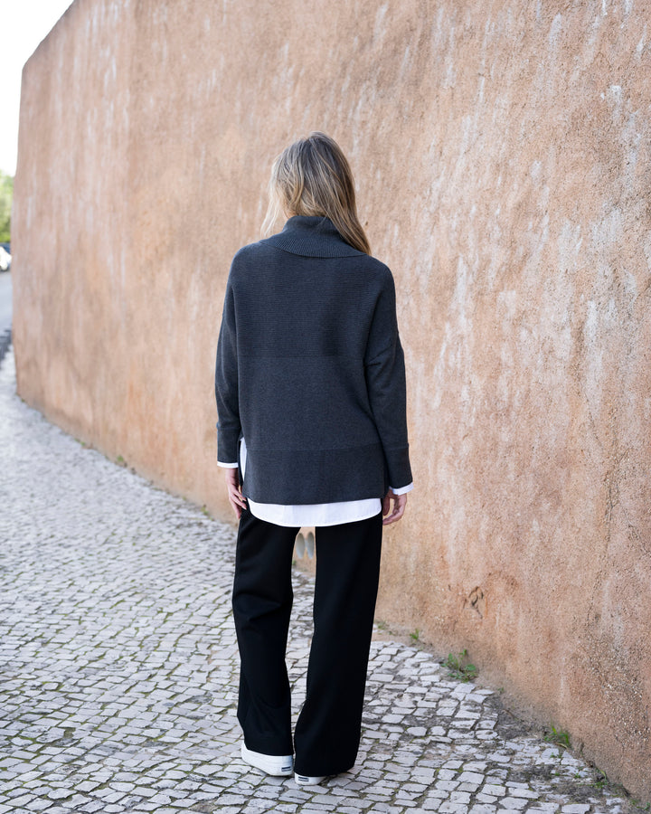 Person wearing a dark coat and black pants walking away from a textured wall.