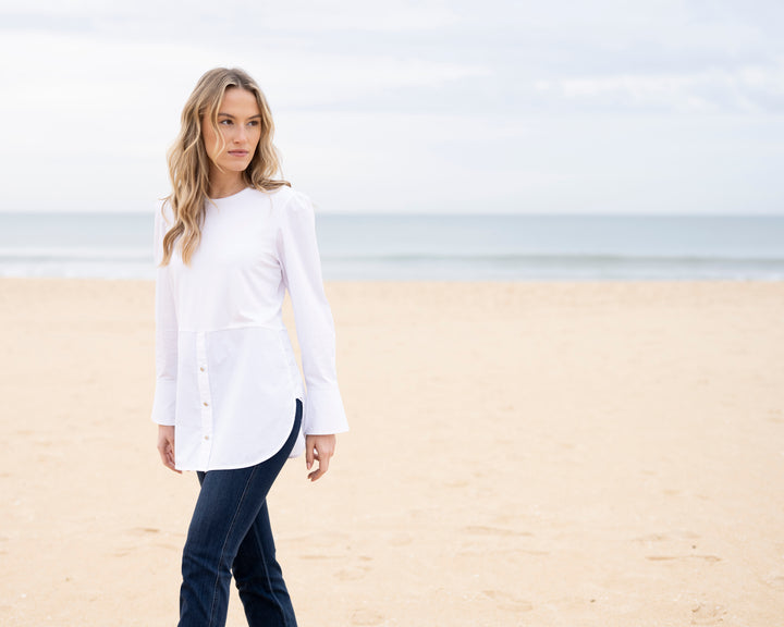 Woman wearing a white shirt and dark pants on a beach