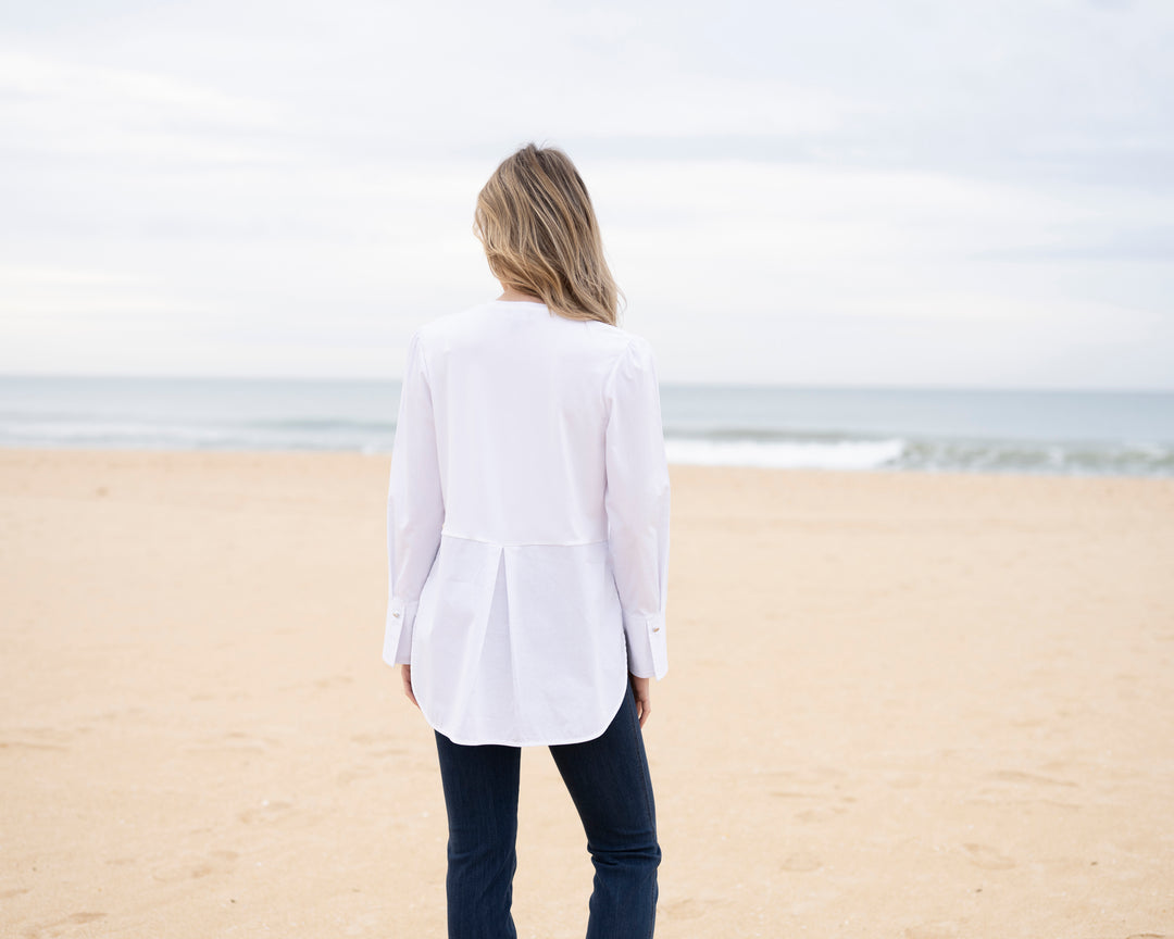 Person standing on a beach wearing a white shirt and dark pants, facing away from the camera.