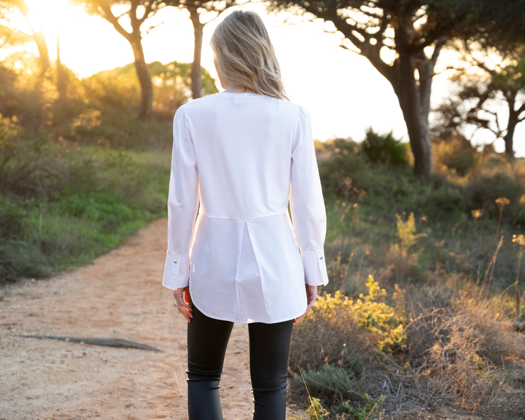 Person wearing a white shirt and black pants walking on a dirt path in a natural setting.