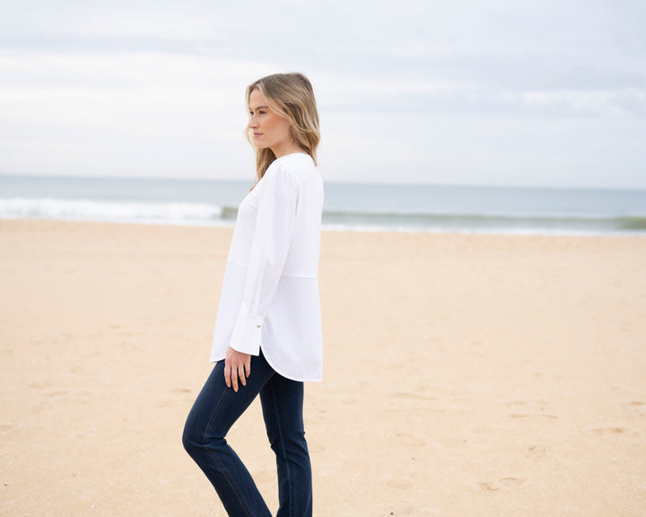 Woman in a white shirt and dark jeans standing on a sandy beach.