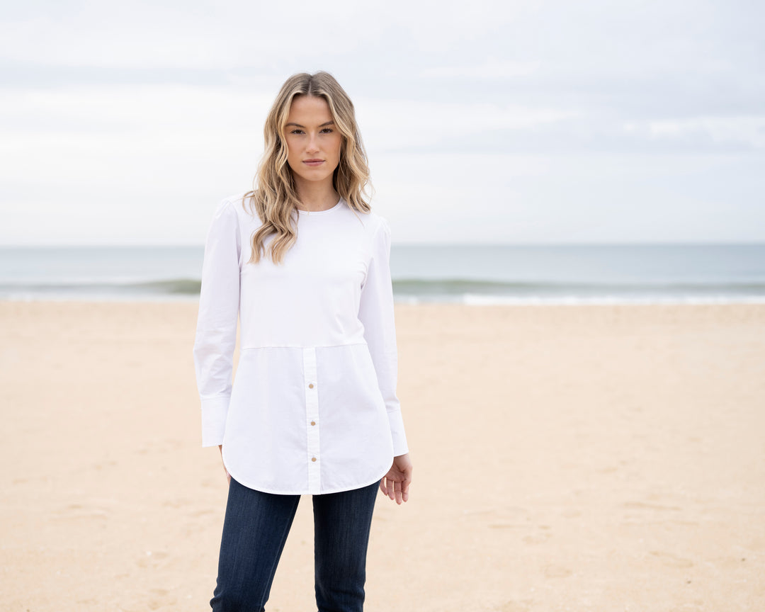 Woman wearing a white shirt and dark pants standing on a beach.