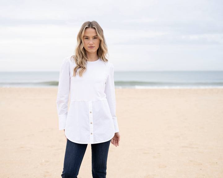 Woman wearing a white shirt and dark pants standing on a beach.