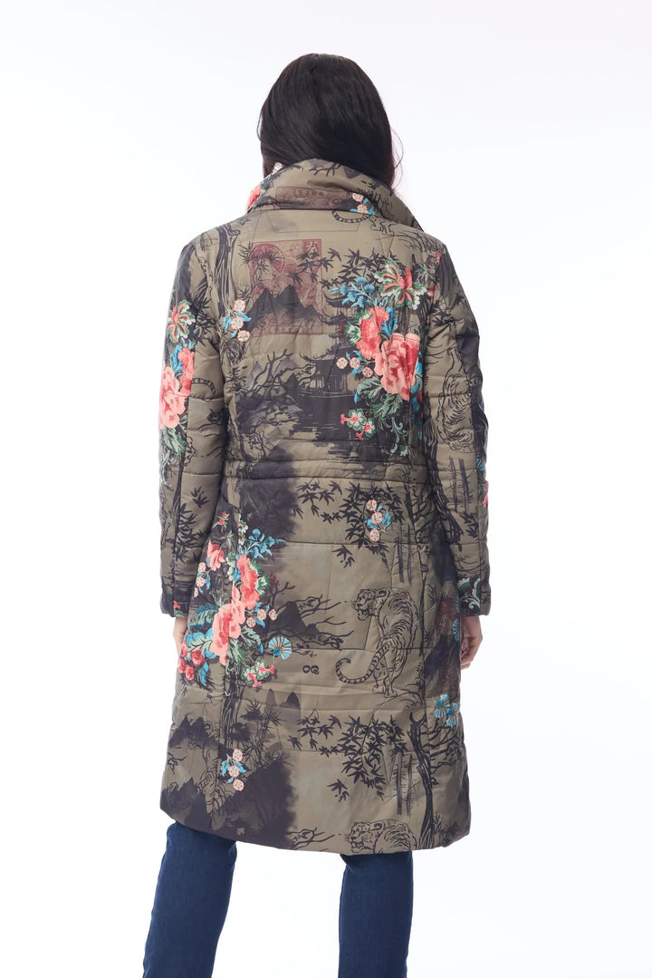 A person shown from the back wearing a long quilted coat with a scenic landscape print and colorful floral accents, paired with dark blue pants and white sneakers, against a plain white studio background.