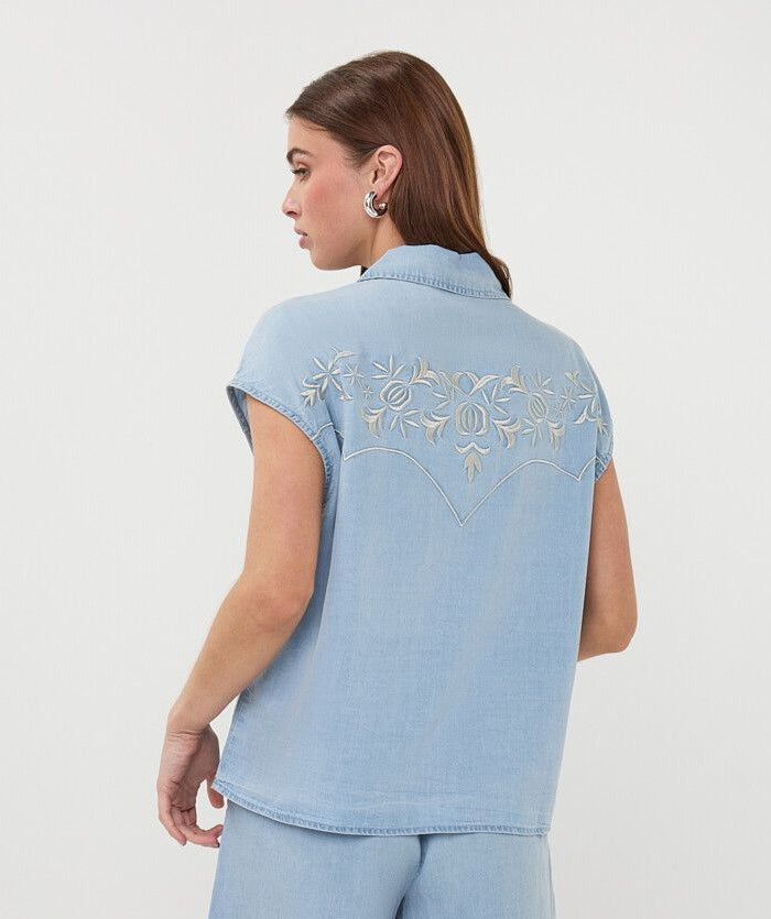 Woman wearing a light blue denim outfit with floral embroidery on a white background