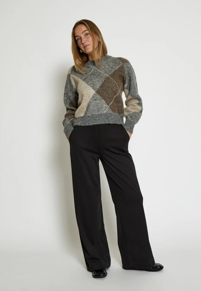 Woman wearing a patterned sweater and black pants on a white background