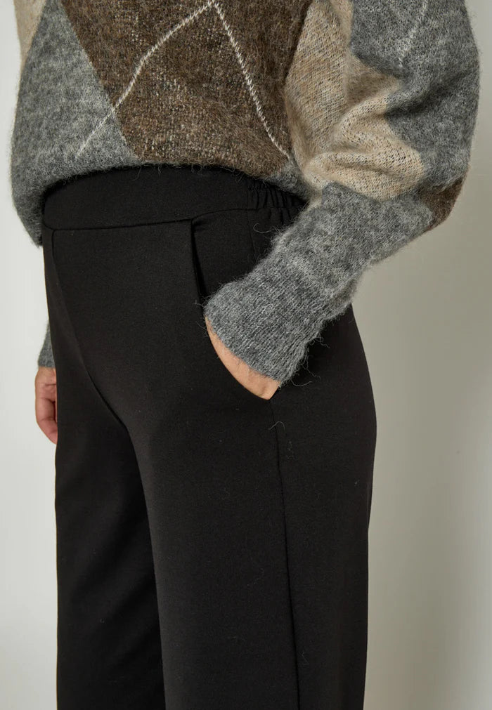 Person wearing a patterned sweater and black pants against a neutral background