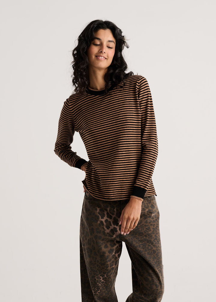 A woman modeling a brown and black horizontally striped long-sleeve top with wide-leg brown pants featuring a subtle leopard print, standing against a light gray studio background.