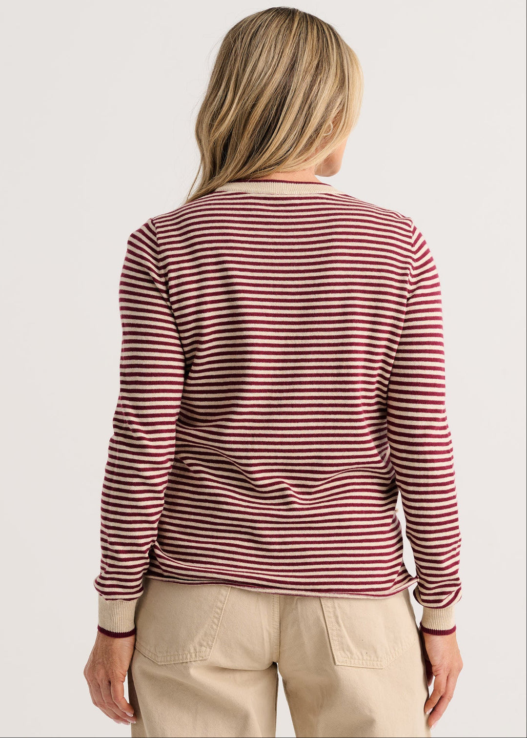 A woman viewed from the back wearing a long-sleeve crewneck top with horizontal burgundy and beige stripes, paired with beige pants, against a light gray studio background.