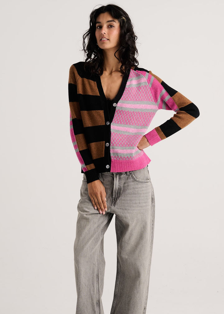 A model stands against a light gray studio background wearing a colorful knit cardigan with brown, black, pink, and white stripes, paired with light gray wide-leg jeans and brown shoes.