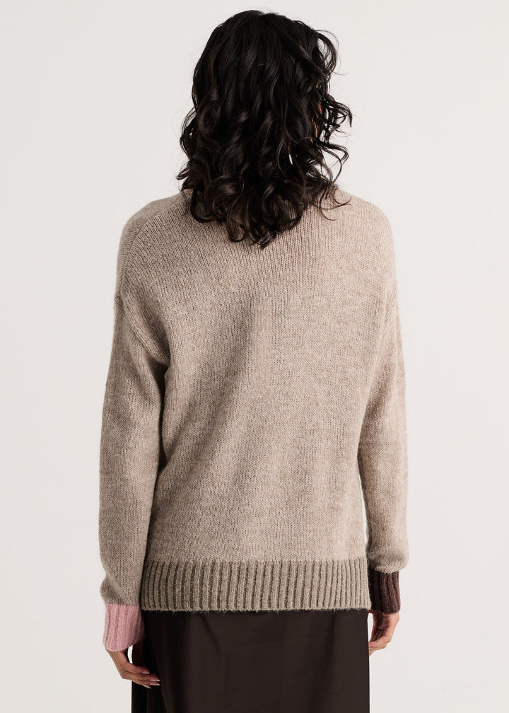A woman viewed from the back wearing a light beige knit sweater with dark brown cuffs and a dark brown skirt, set against a plain light gray background.