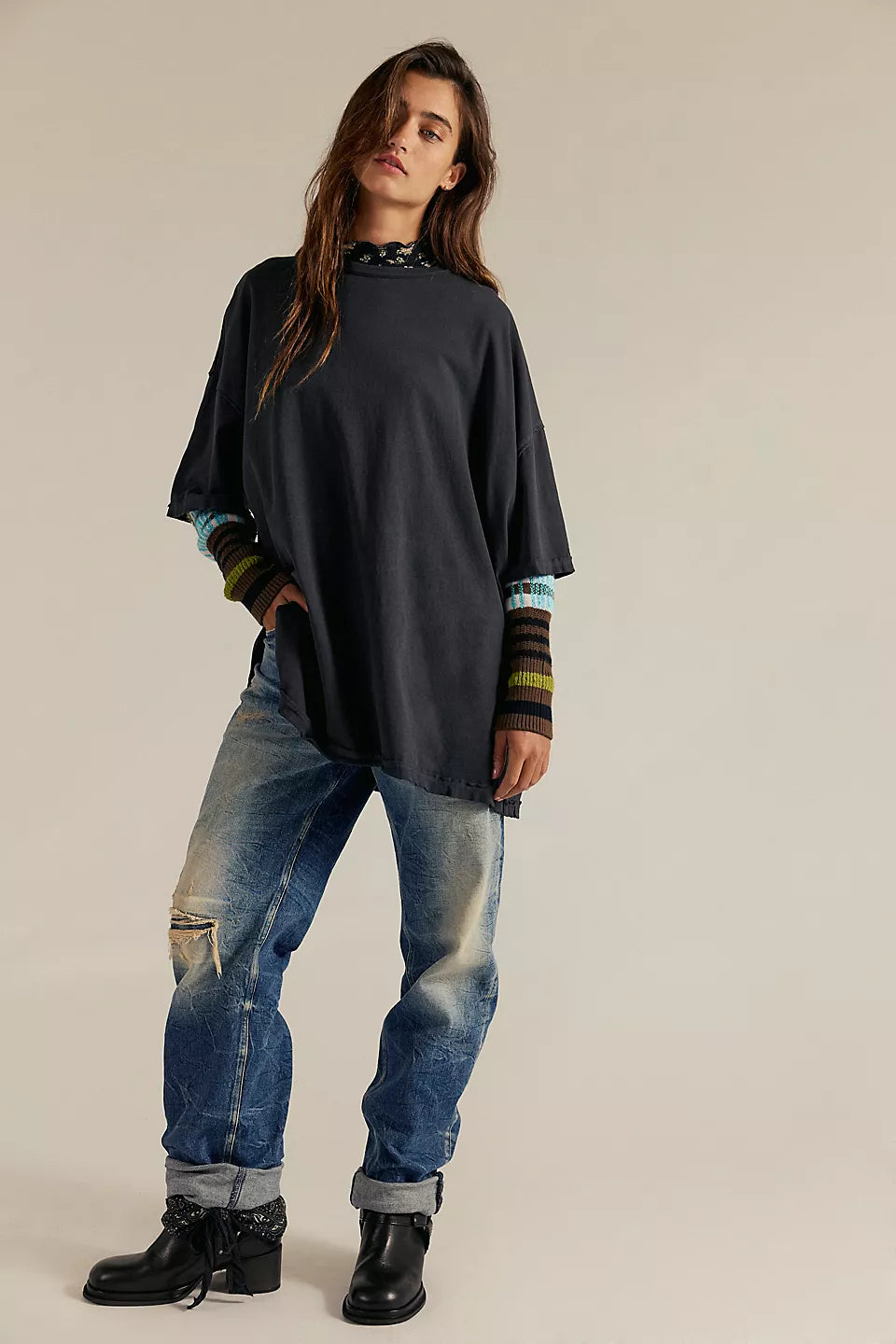 Woman wearing a black oversized sweater with colorful cuffs and blue jeans on a beige background