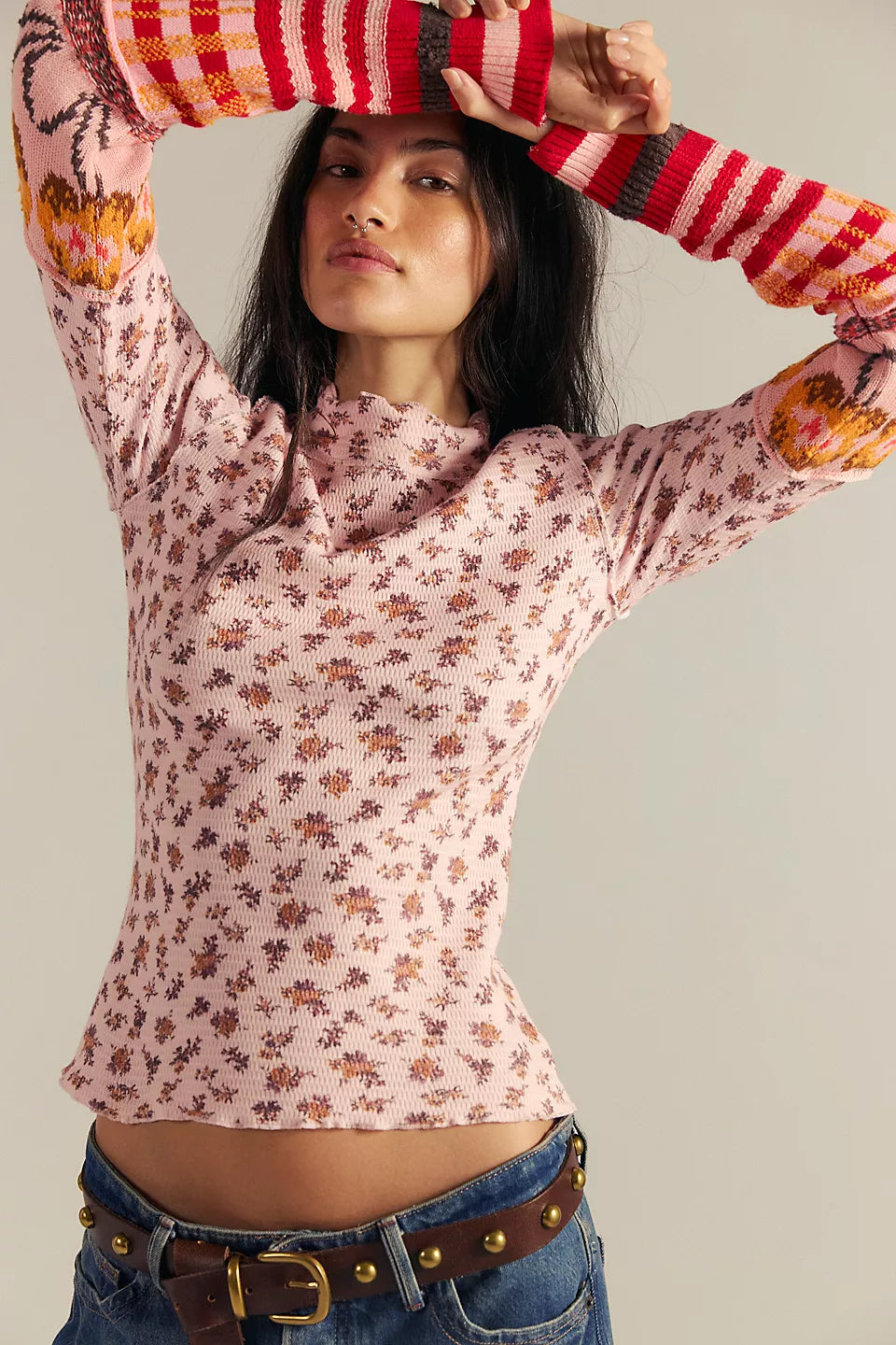 Woman wearing a pink floral long-sleeve top and blue jeans against a neutral background