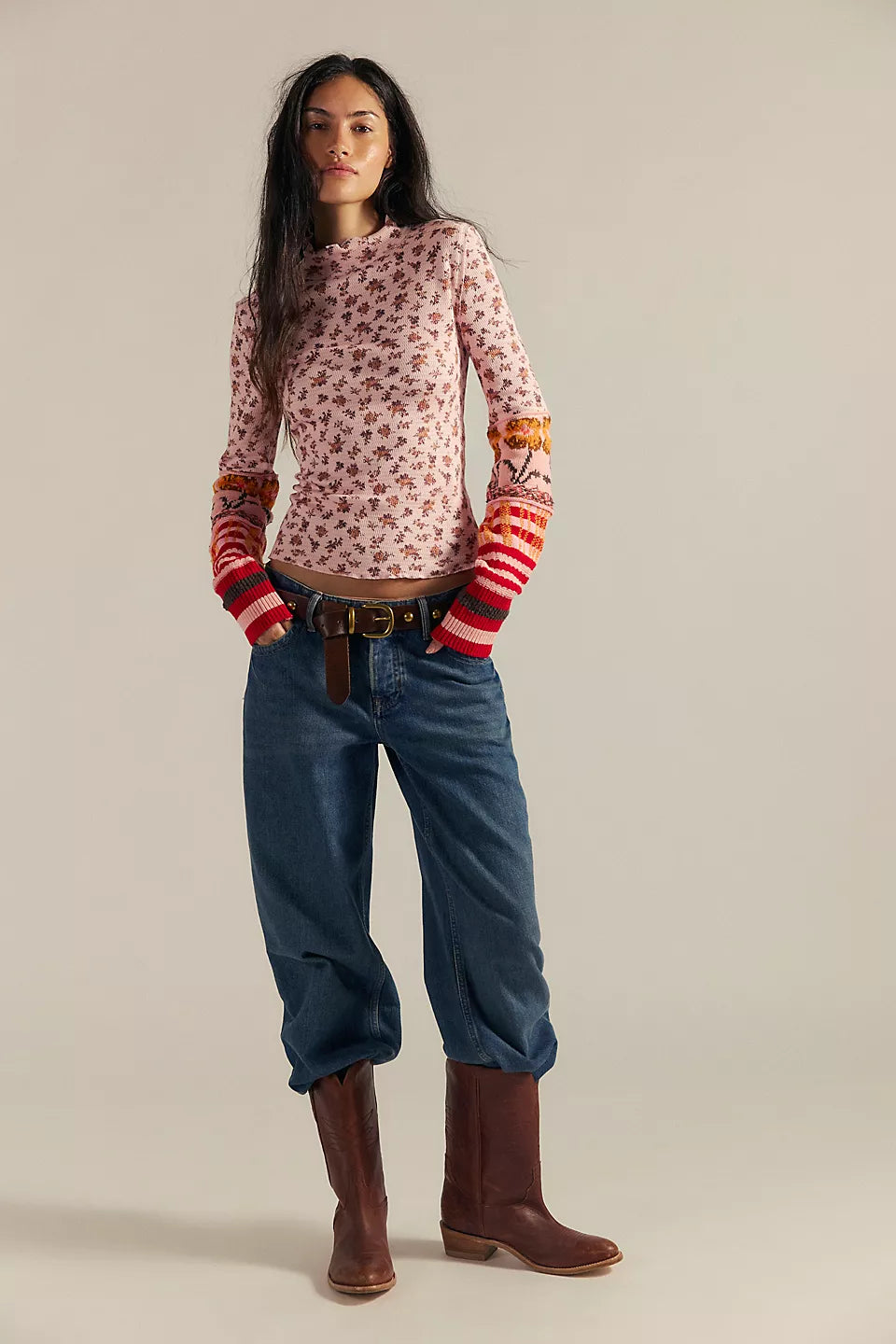 Woman wearing a patterned sweater, jeans, and brown boots on a beige background