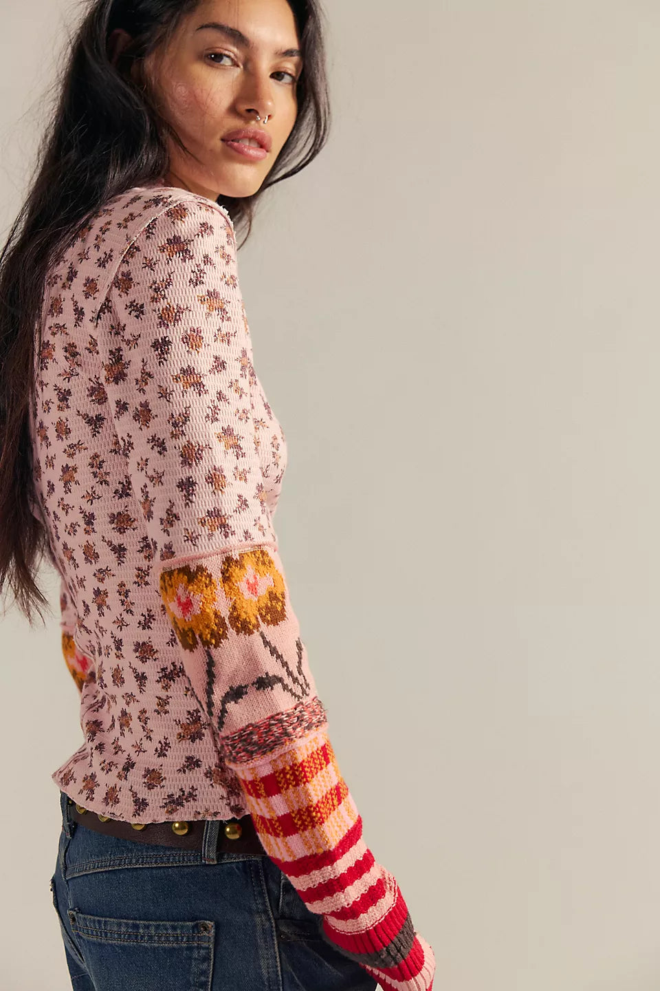 Woman wearing a floral long-sleeve top with colorful sleeves on a plain background