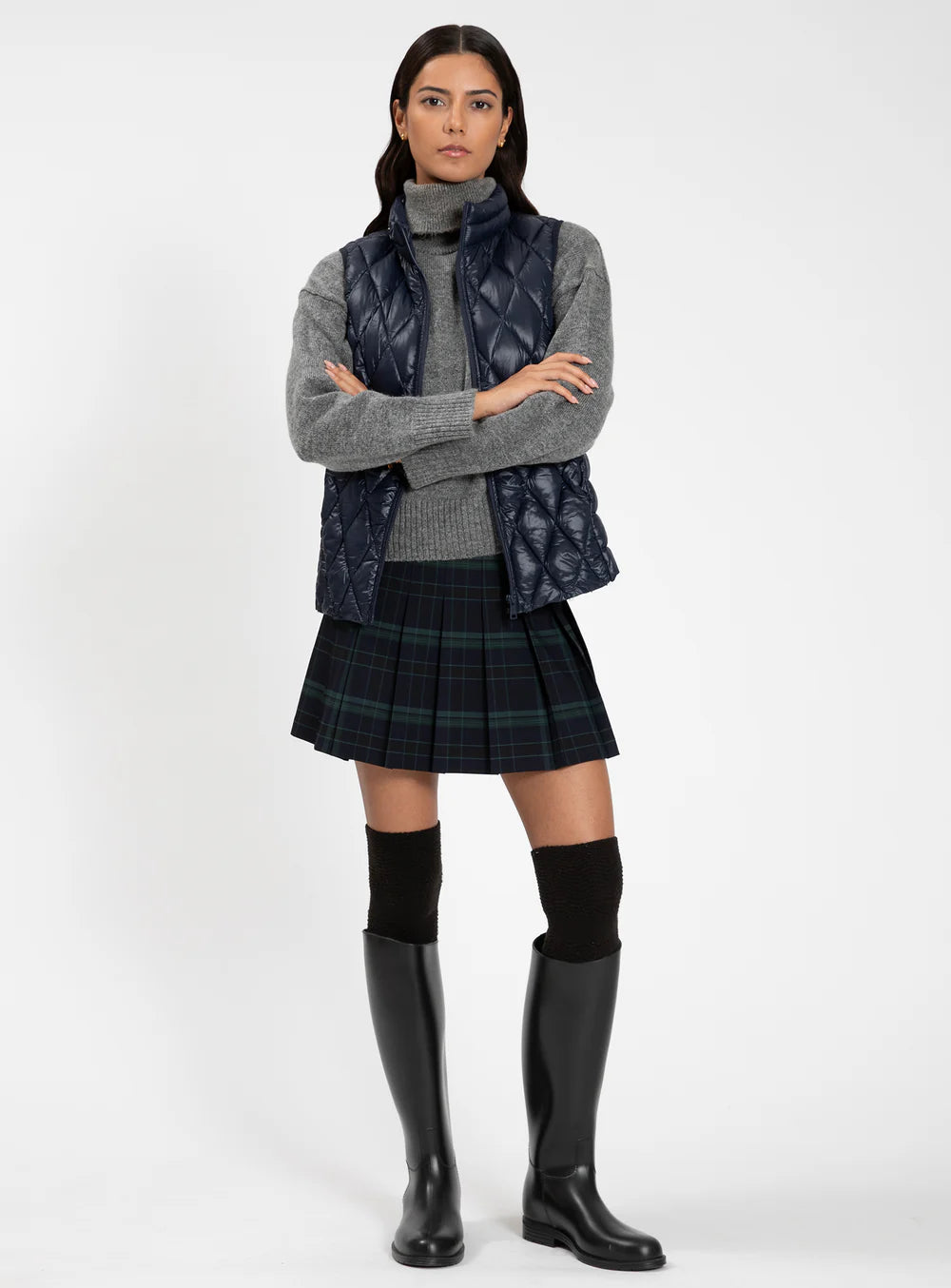 Woman wearing a gray sweater, plaid skirt, and black rain boots on a white background