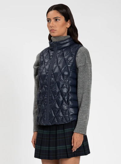 Woman wearing a quilted navy vest over a gray sweater and plaid skirt on a white background
