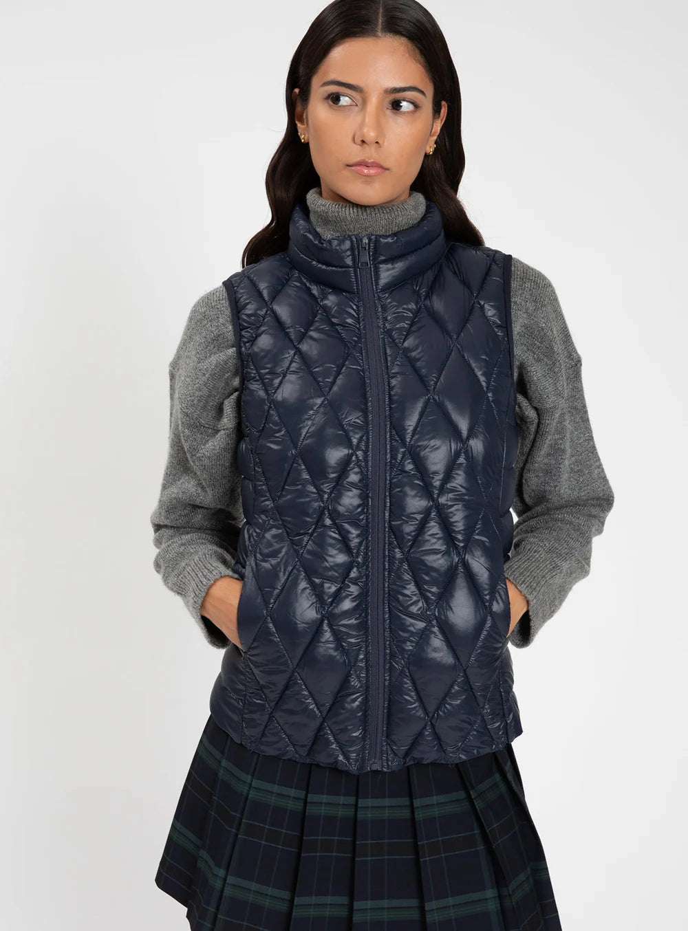 Woman wearing a navy quilted vest over a gray sweater on a white background