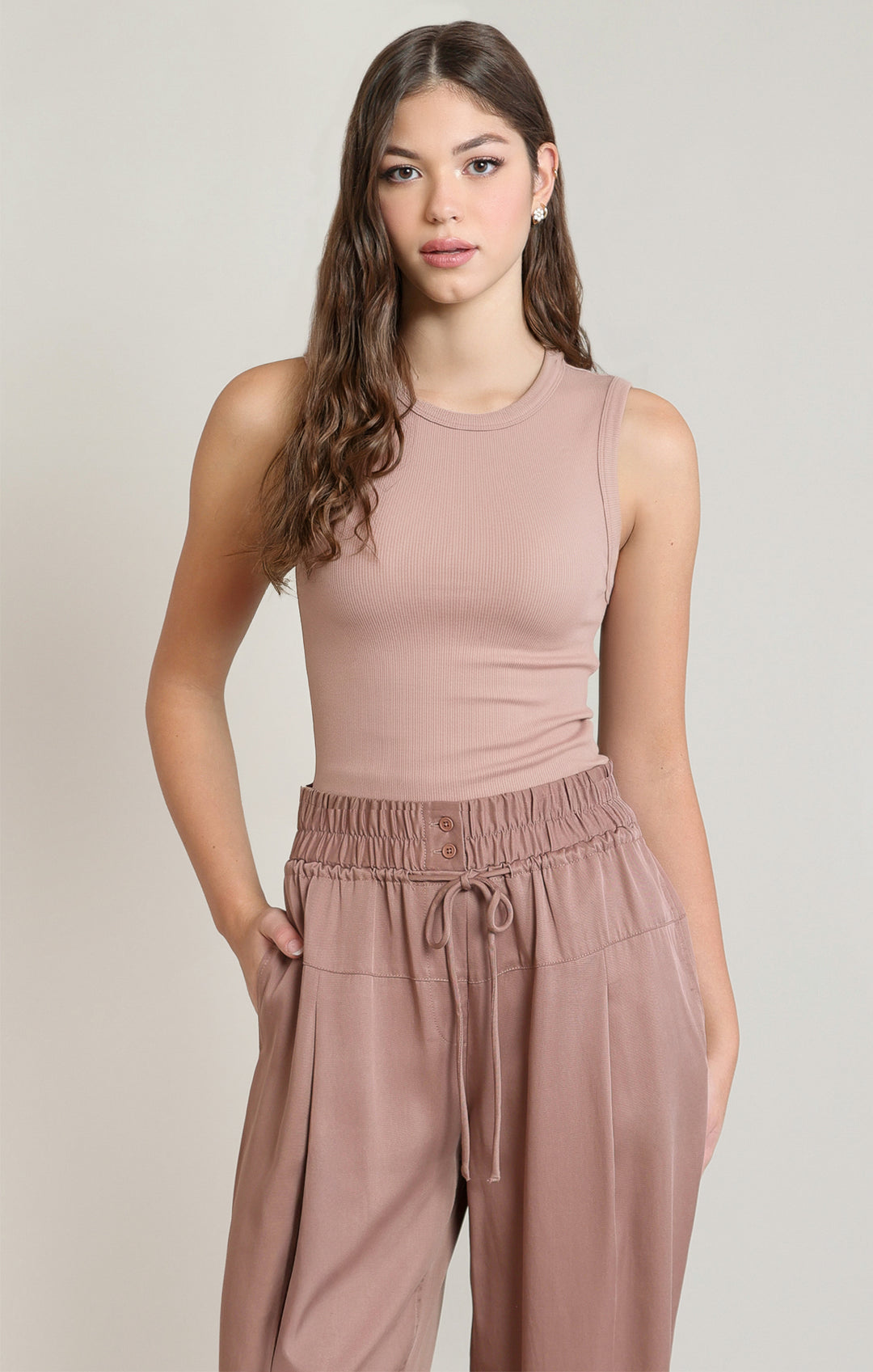 Woman wearing a matching sleeveless top and wide-leg pants in a neutral color on a plain background