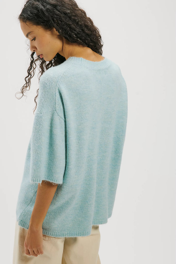 A woman wearing a light blue-green knit sweater, shown from the back against a plain white studio background.