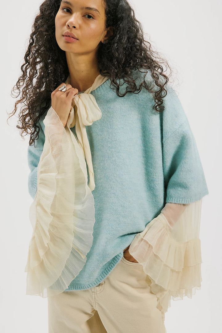 Woman wearing a light blue poncho with beige accents on a white background