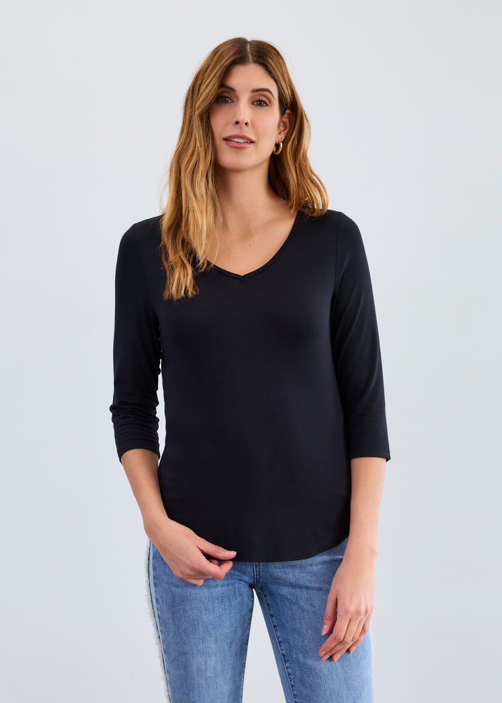 Woman wearing a black long-sleeve top and blue jeans on a light gray background