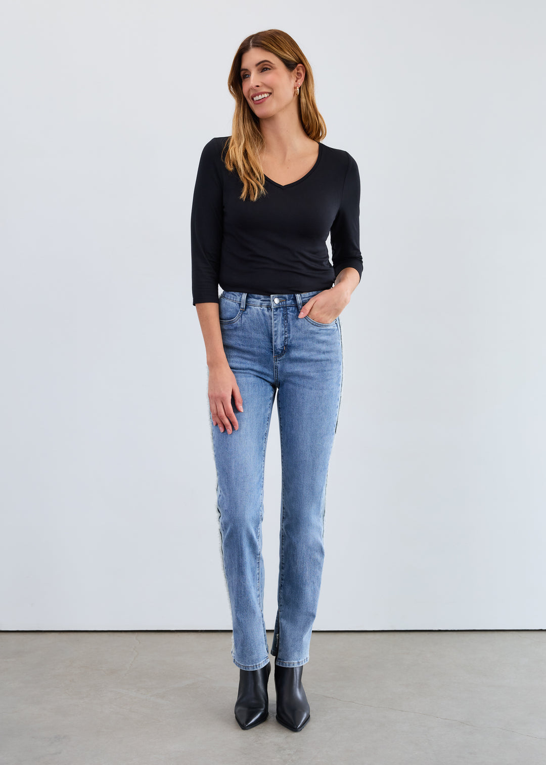 Woman wearing a black top and light blue jeans against a white background