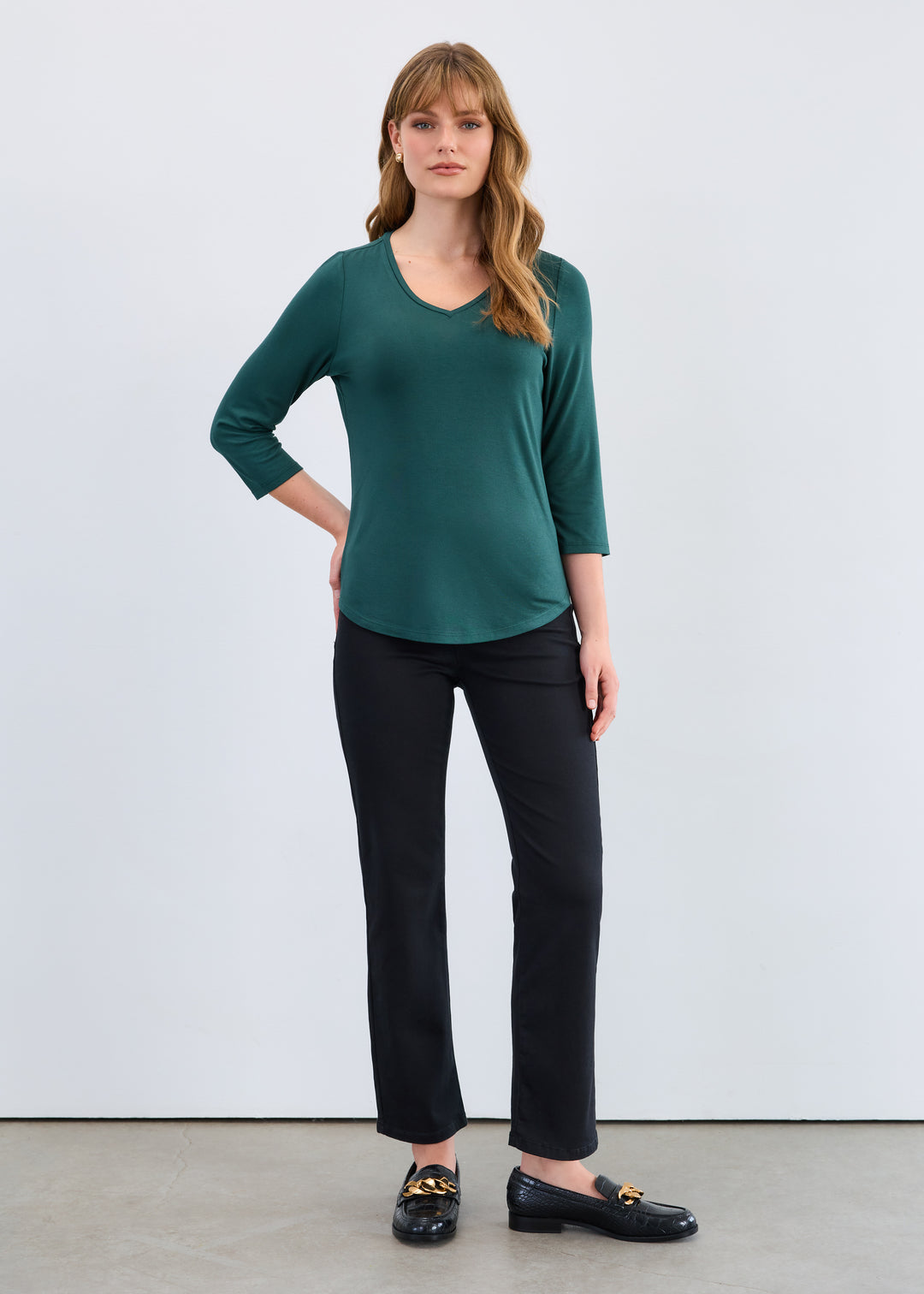 Woman wearing a green top and black pants against a white background