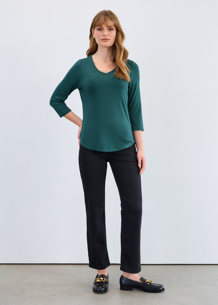 Woman wearing a green top and black pants against a white background