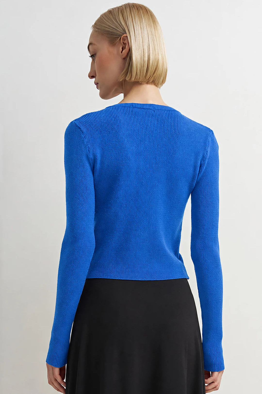 Woman wearing a blue long-sleeve top and black skirt on a light gray background