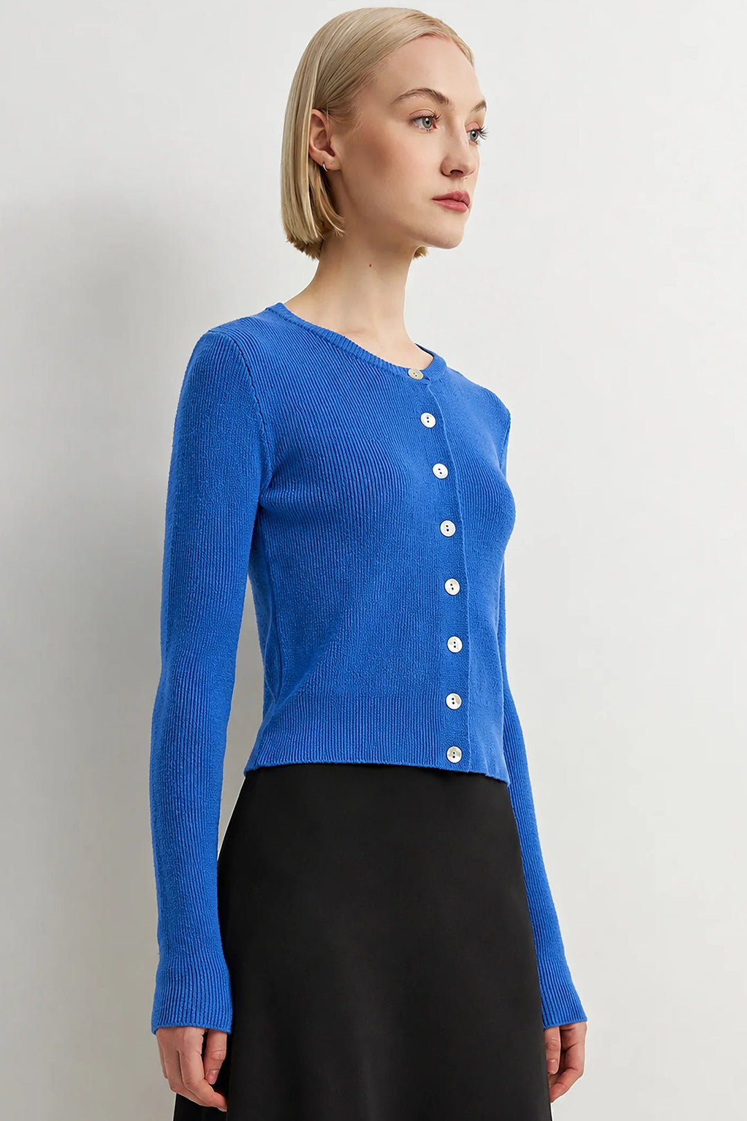 Woman wearing a blue cardigan with white buttons against a plain background