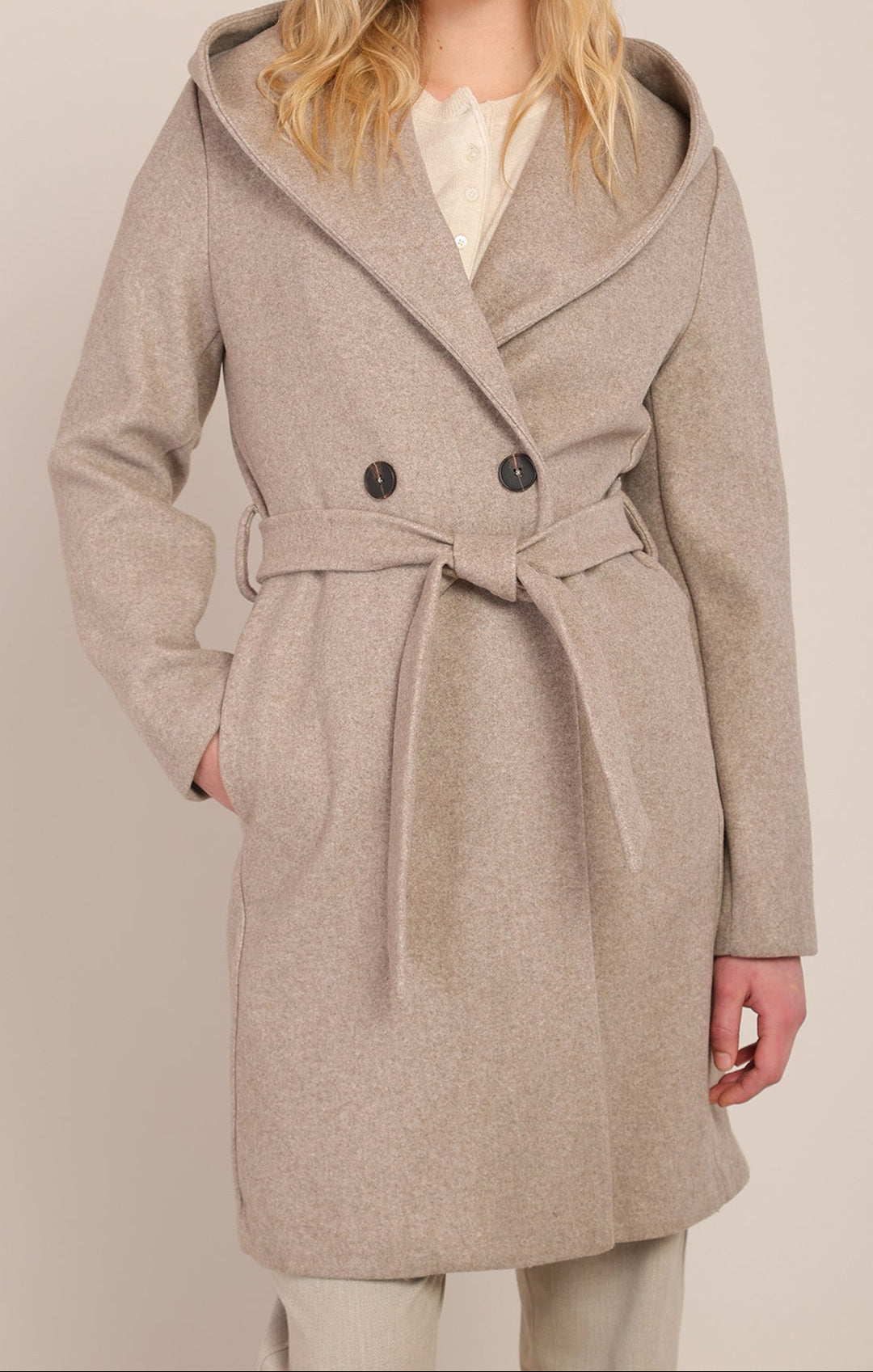 Woman wearing a beige coat with a hood on a plain background