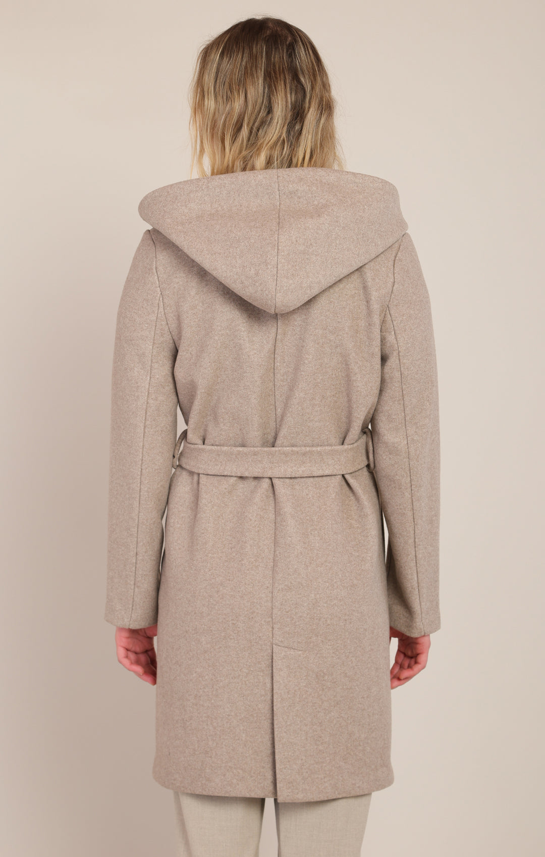 Woman wearing a beige hooded coat on a plain background