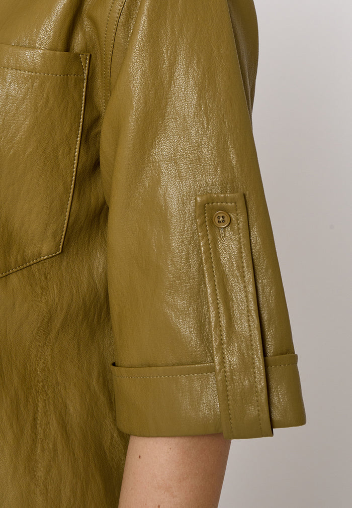 Close-up of a person wearing a textured olive green shirt, showing the sleeve with a buttoned pocket detail and a chest pocket.