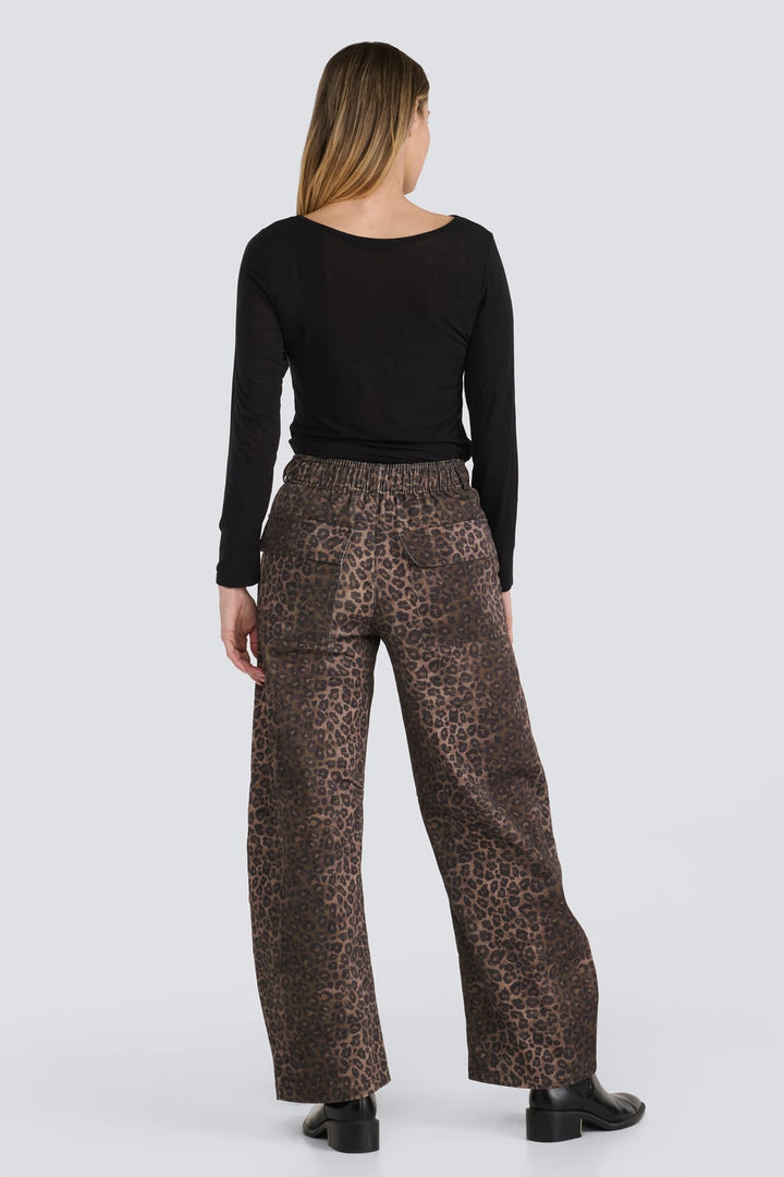 A woman is shown from the back wearing a black long-sleeve top and brown leopard-print wide-leg trousers, standing against a light gray studio background.