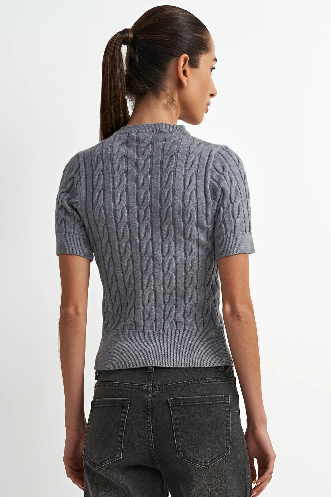 Woman wearing a gray cable knit sweater and dark jeans on a white background