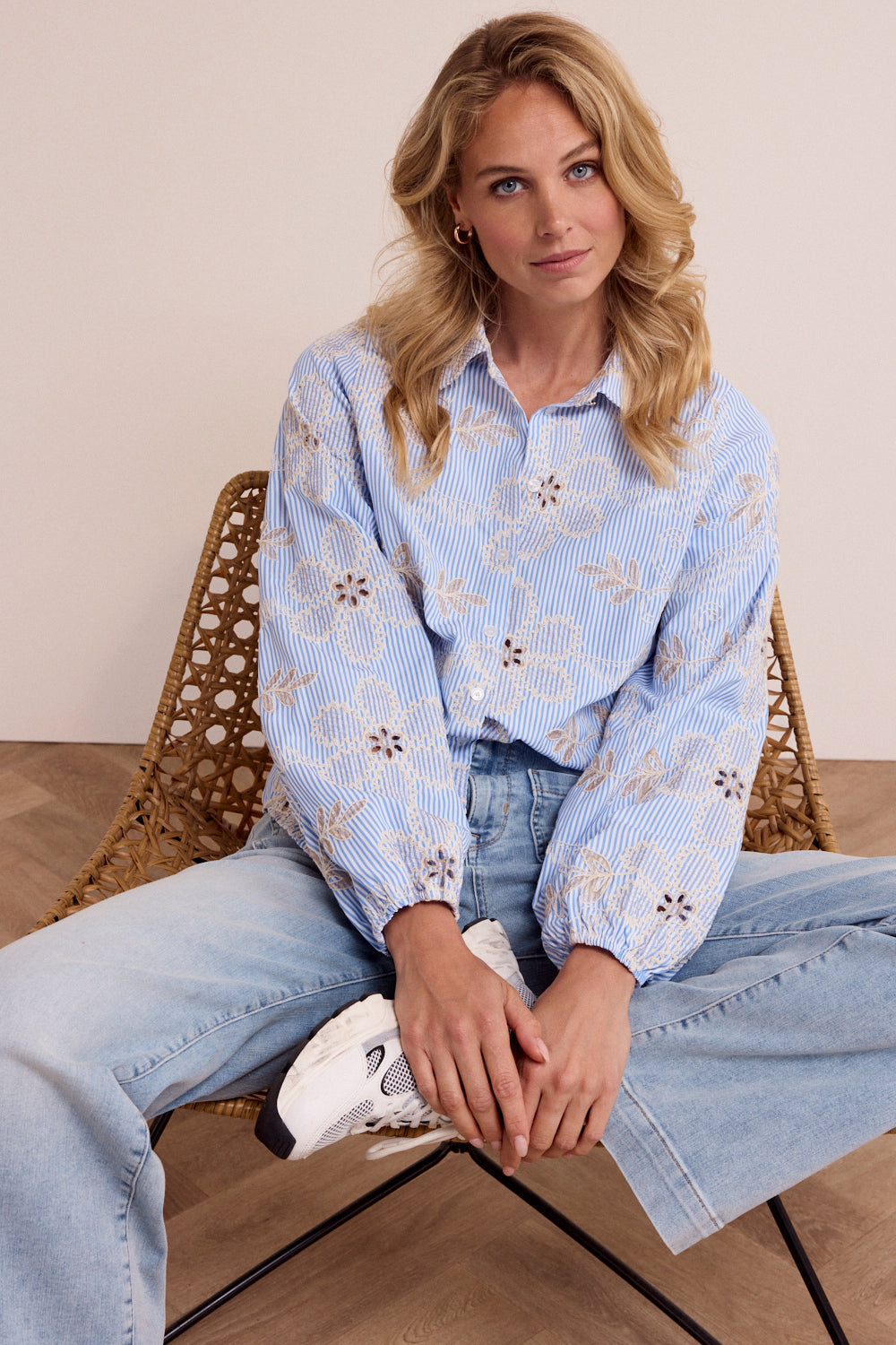 Woman sitting on a chair wearing a light blue patterned shirt and jeans.