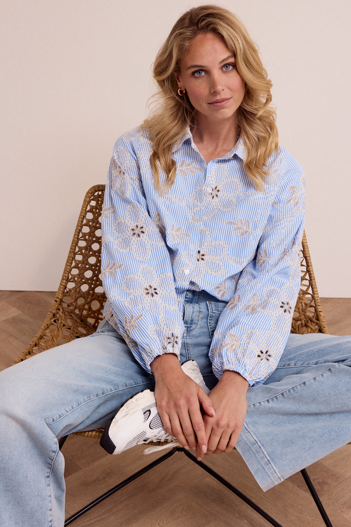 Woman sitting on a chair wearing a light blue patterned shirt and jeans.