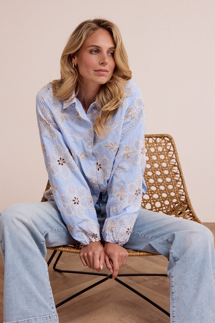 Woman sitting on a chair wearing a light blue patterned shirt and jeans.