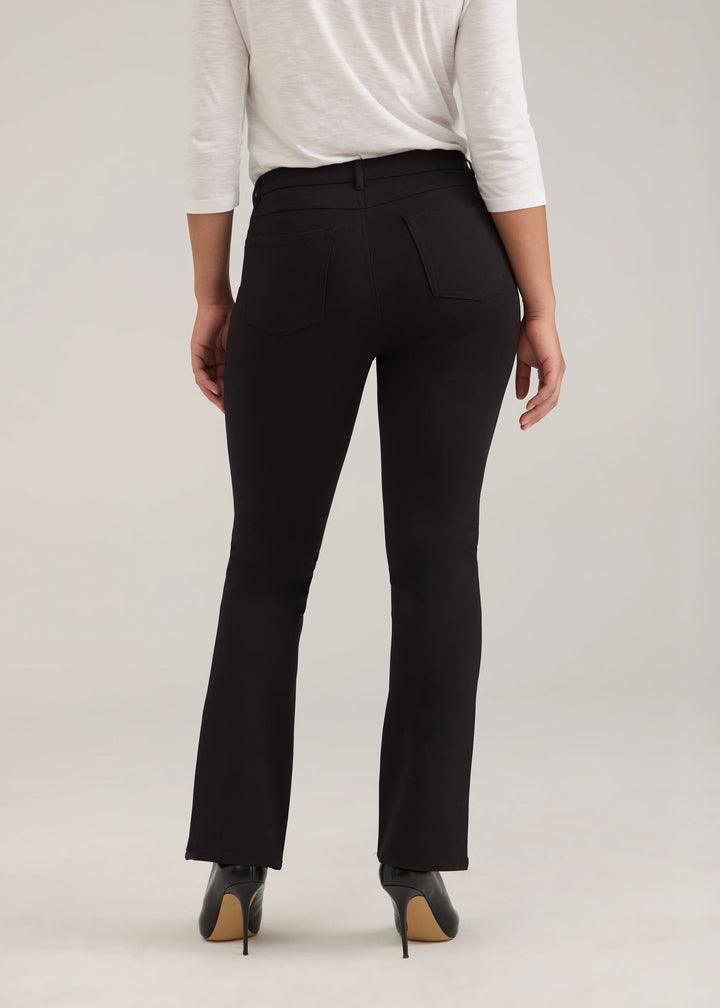 A model shown from the back wearing black high-waisted flared trousers, a white long-sleeve top, and black high-heeled shoes against a light gray studio background.
