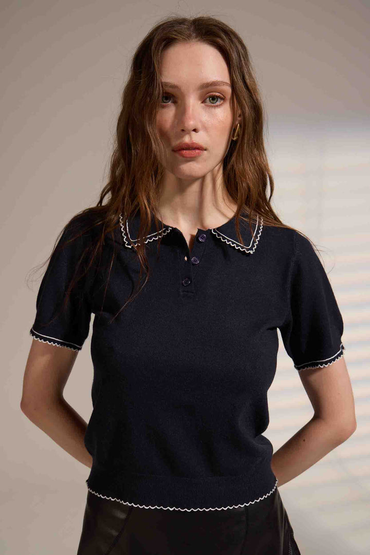 Woman wearing a dark blue polo shirt with white trim against a neutral background