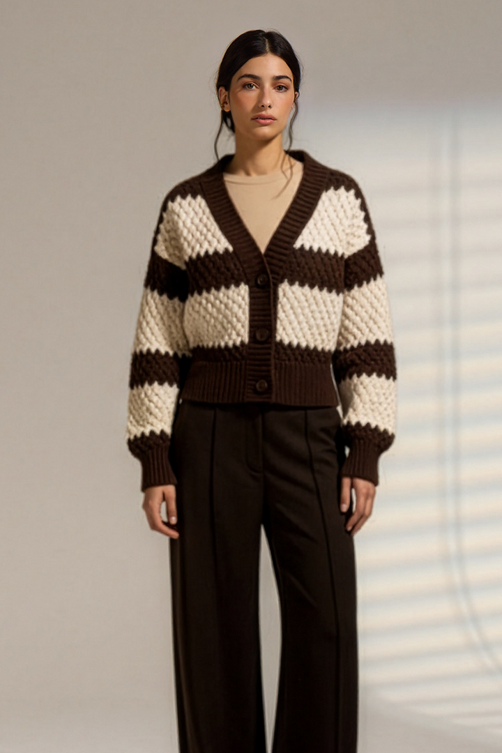 A model stands in a studio wearing a brown and cream striped knit cardigan with a belted waist, paired with dark wide-leg trousers.