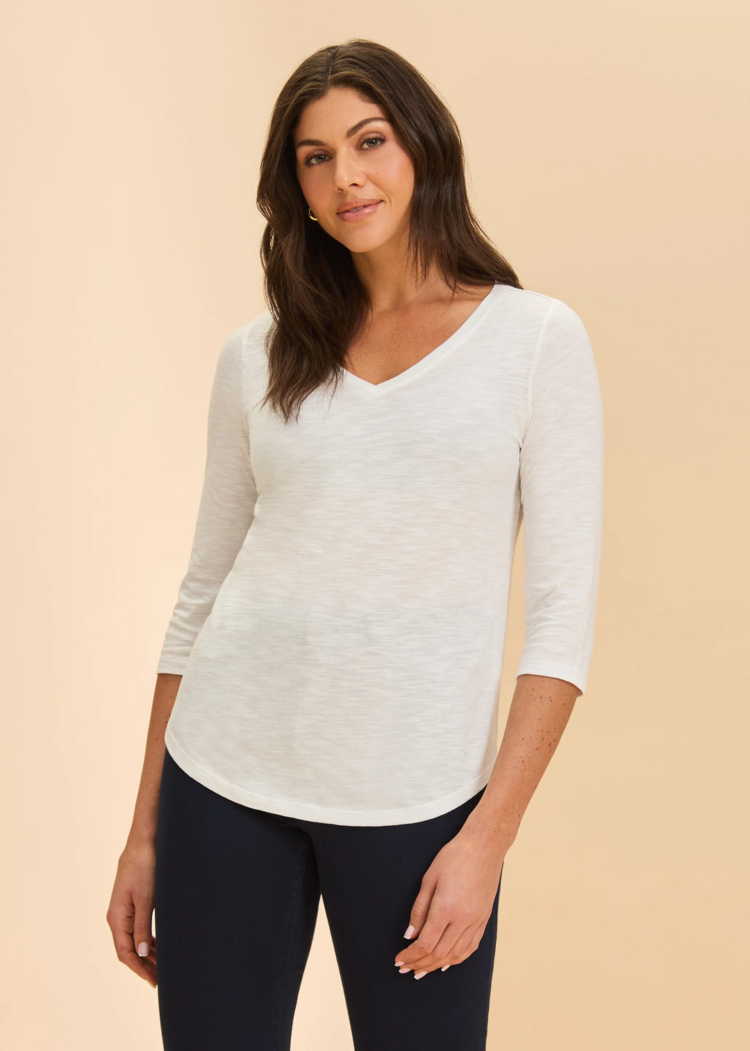 Woman wearing a white long-sleeve top and dark pants on a beige background