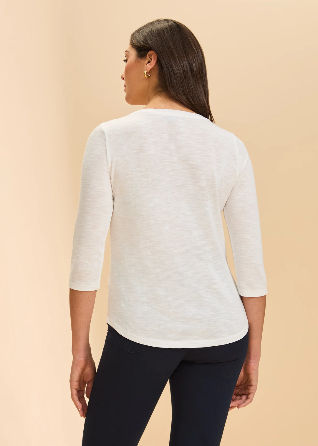 Woman wearing a white sweater with 3/4 sleeves on a beige background