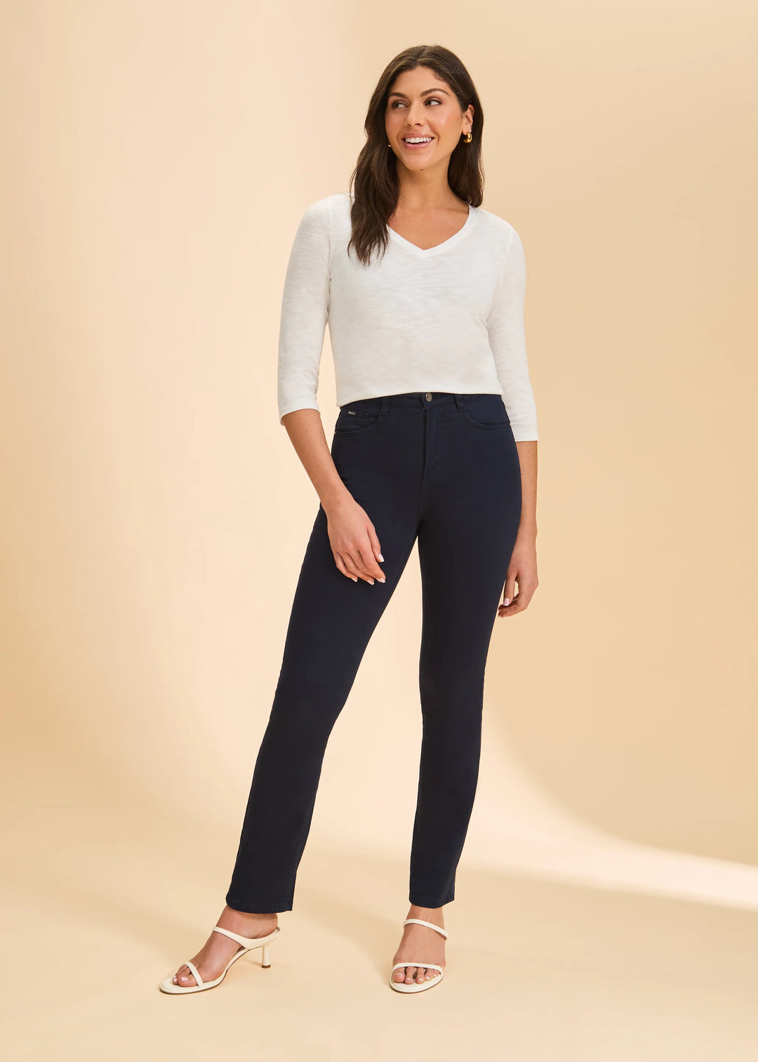 Woman wearing a white top and navy pants on a beige background