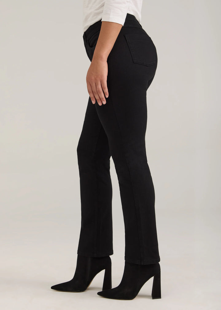 A side view of a model wearing black flared pants, a white top, and black high-heeled ankle boots against a light gray studio background.