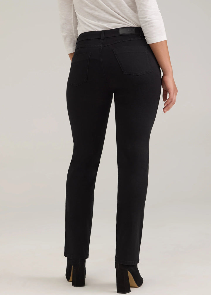 Rear view of a model wearing black slim-fit ankle-length pants with a black belt, paired with a white long-sleeve top and black heels, against a light gray studio background.
