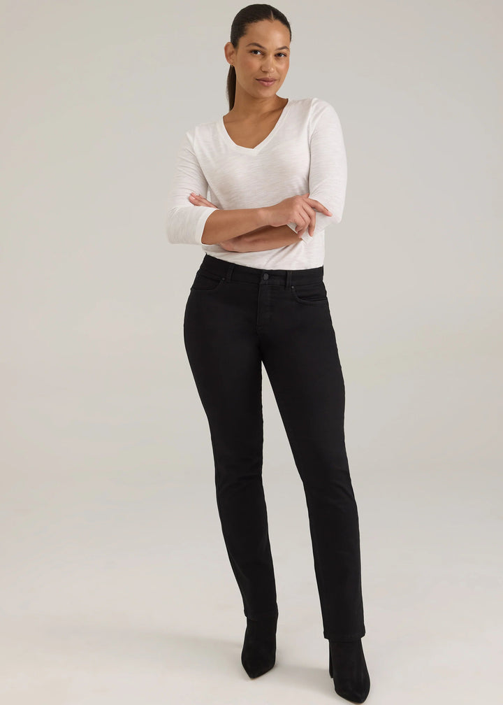 A woman modeling black skinny jeans with a white long-sleeve top, standing against a light gray studio background.