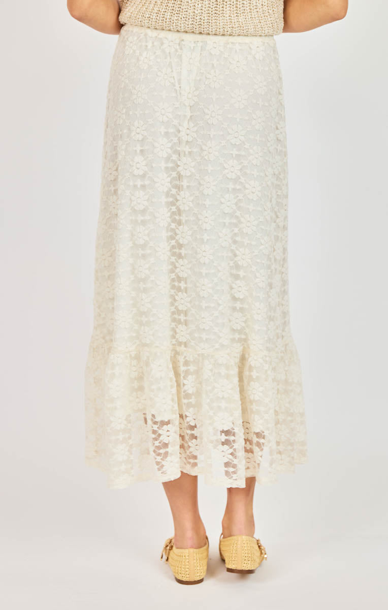 Person wearing a white lace skirt with yellow sandals on a light gray background
